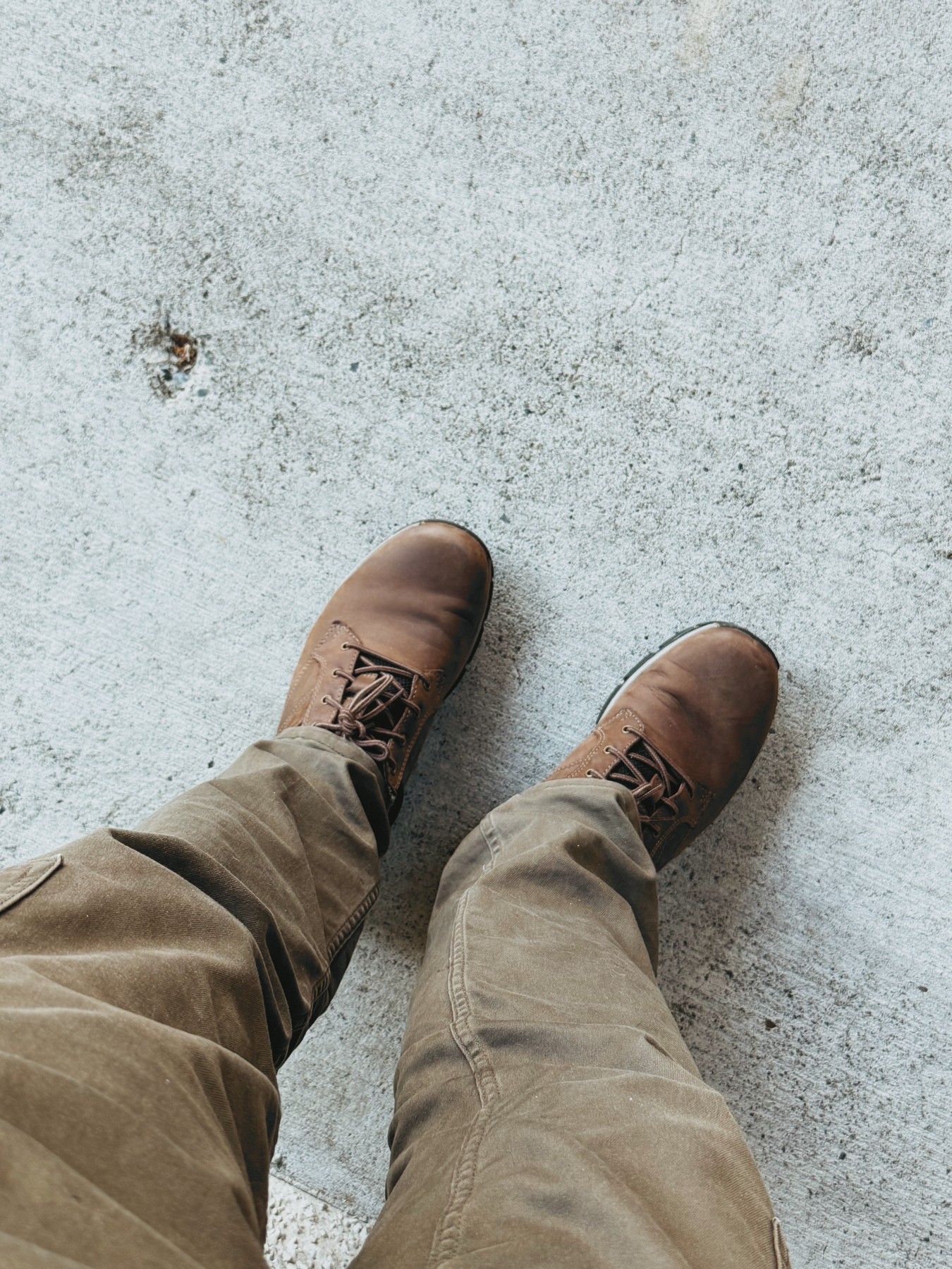 Looking down at brown boots and khaki trousers on pale pavement